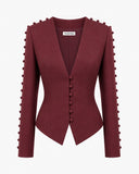 A structured long-sleeve blazer in deep burgundy, featuring a deep V-neckline, a front button closure, and decorative pom-pom detailing along the shoulders and sleeves, shown against a plain white background.